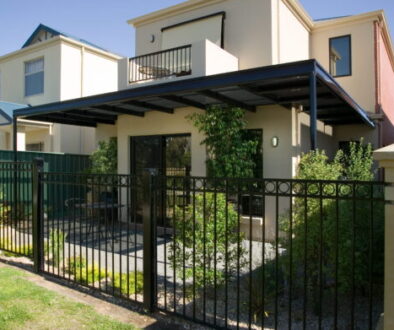 Dark-framed Stratco Outback pergola with shadecloth over a courtyard at a two-storey rendered home