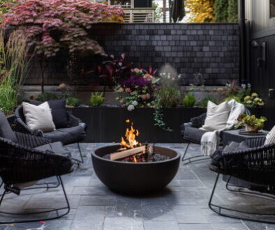 A modern outdoor patio with cosy seating, potted plants and a fire pit creating a welcoming backyard gathering space